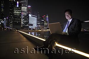Asia Images Group - Mature man working on a laptop at night, buildings as background