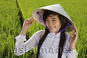 Asia Images Group - Young woman wearing traditional Vietnamese hat standing in rice paddy