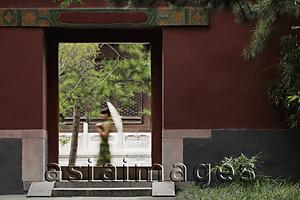 Asia Images Group - Young woman walking by Chinese doorway holding an umbrella