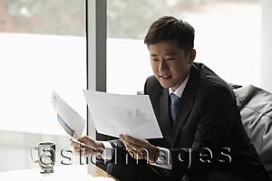 Asia Images Group - Young man in a suit looking at papers in an office