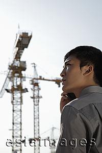 Asia Images Group - profile of young man holding phone standing in front of construction site