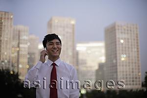 Asia Images Group - Young man talking on phone in front of buildings in the evening, China
