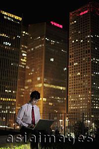 Asia Images Group - Young man working on his lap top with buildings as backdrop