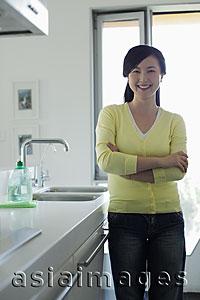 Asia Images Group - Young woman smiling in kitchen with arms crossed