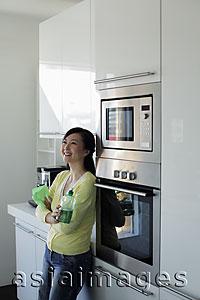 Asia Images Group - Young woman standing in kitchen looking up and smiling