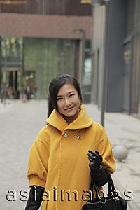 Asia Images Group - Young woman wearing yellow coat and gloves shopping outdoors