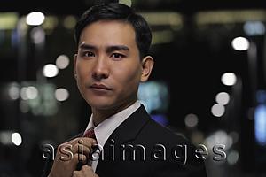 Asia Images Group - Man in business suit straightening his tie at night