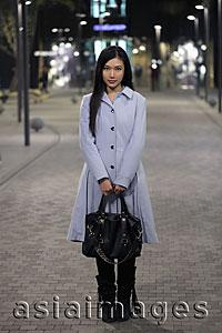 Asia Images Group - Young woman standing on the street holding her purse, at night
