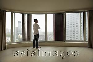 Asia Images Group - Rear view of young man looking out large windows of condo