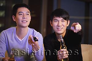 Asia Images Group - Young men watching TV together and holding bottles of beer