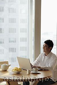 Asia Images Group - Young man sitting at a table working on a laptop computer