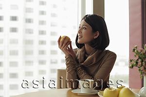 Asia Images Group - Young woman holding apple and looking out window