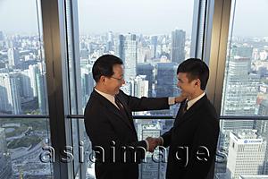 Asia Images Group - Two men shaking hands in front of window with a view of the city of Beijing
