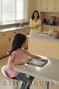 Asia Images Group - Mother watching her daughter play on a digital tablet as she cooks