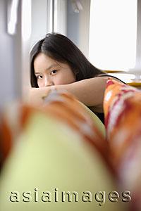 Asia Images Group - Young woman peering out from behind her arm, pillows in foreground