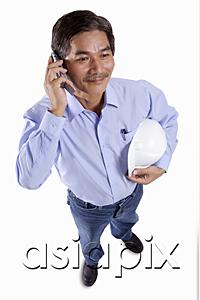 AsiaPix - Mature man holding construction hat, using mobile phone