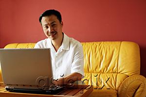 AsiaPix - Man sitting on sofa, using laptop, looking at camera, portrait