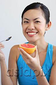 AsiaPix - Woman holding grapefruit and spoon, looking at camera