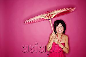 AsiaPix - Woman holding umbrella, standing against pink background