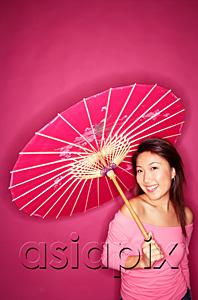 AsiaPix - Woman holding umbrella, wearing pink top, standing against pink background