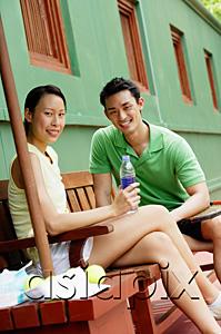 AsiaPix - Couple sitting on bench on tennis court, smiling at camera, woman holding water bottle