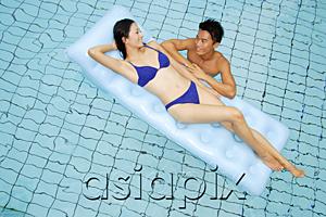 AsiaPix - Woman lying on pool raft, smiling at man in water next to her