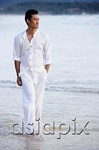AsiaPix - Man walking on beach, hand in pocket, ankle deep in water
