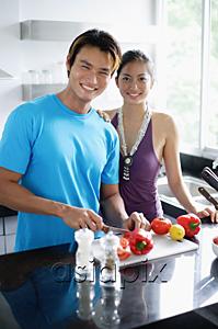 AsiaPix - Couple standing in kitchen, looking at camera, man holding knife, chopping vegetables