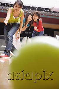 AsiaPix - Young woman bowling, friends watching behind her