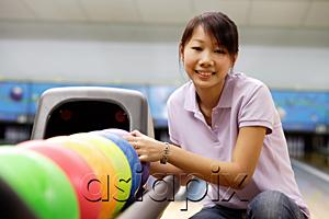 AsiaPix - Woman selecting ball at bowling alley, smiling at camera