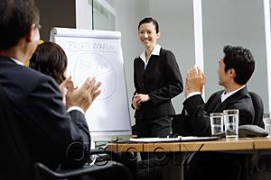 AsiaPix - Businesswoman standing next to flipchart, other executives clapping