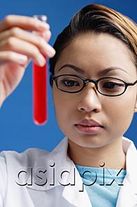 AsiaPix - Female technician looking at test tube filled with red liquid