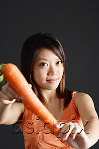 AsiaPix - Young woman holding carrot, looking at camera