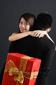 AsiaPix - Man holding gift behind his back, woman embracing him, looking over shoulder at camera