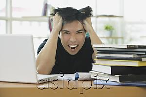 AsiaPix - Young adult with laptop and books, hands in hair, grimacing