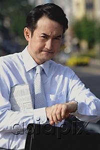 AsiaPix - Businessman with newspaper under his arm, looking at watch, frowning