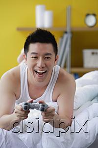 AsiaPix - Man lying on bed, playing video game