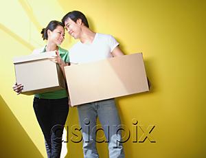 AsiaPix - Couple carrying boxes, standing against yellow wall