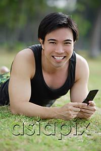 AsiaPix - Man lying on grass, holding mobile phone, smiling at camera