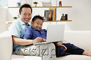 AsiaPix - Father and son in living room with laptop, smiling at camera