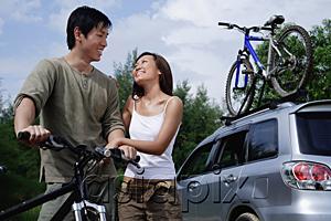 AsiaPix - Man on a bike, woman standing next to him, Sports Utility Vehicle in the background