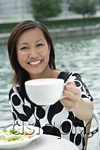 AsiaPix - Young woman holding cappuccino cup, towards camera