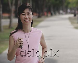 AsiaPix - Mature woman walking in park, listening to MP3 player