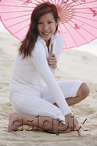 AsiaPix - Young woman holding pink umbrella, kneeling on beach