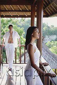 AsiaPix - Young woman in balcony looking away, man standing in background