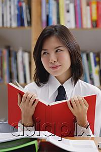 AsiaPix - Young woman in library, holding book, looking away
