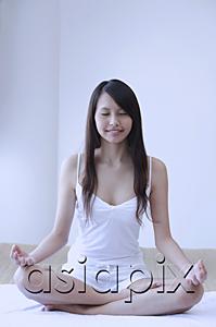AsiaPix - Young woman sitting in yoga position, meditating