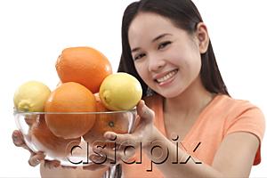 AsiaPix - Young woman holding bowl of oranges and lemons towards camera