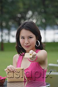 AsiaPix - Young woman sitting at outdoor table, holding credit card towards camera