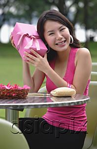 AsiaPix - Woman sitting at outdoor cafe, holding gift to ear